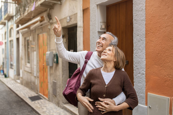引退旅行。陽気な熟女旅行者カップルがバックパックを背負ったヨーロッパの街では、夫が妻屋外で指を指差して観光をしています。現役引退生活 - 写真・画像