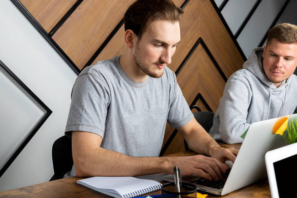 Ein Team von zwei Personen arbeitet im Büro mit einem Computer. IT-Team im Büro mit Laptops, zwei Männer. Online-Assistenten. - Foto, Bild