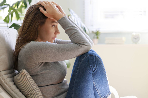 Stressed young woman looking away at window sitting on couch at hom - Foto, immagini
