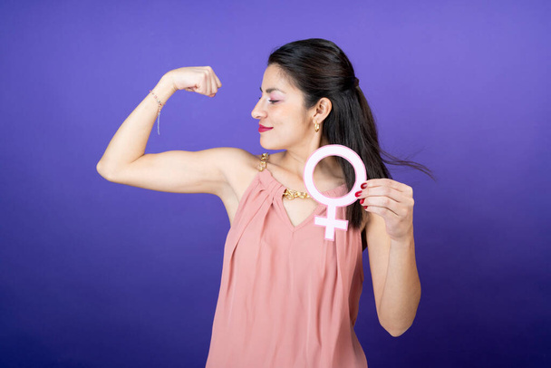kobieta pokazuje swoją siłę na ramieniu trzymając symbol feministyczny w dłoni na odosobnionym tle - Zdjęcie, obraz