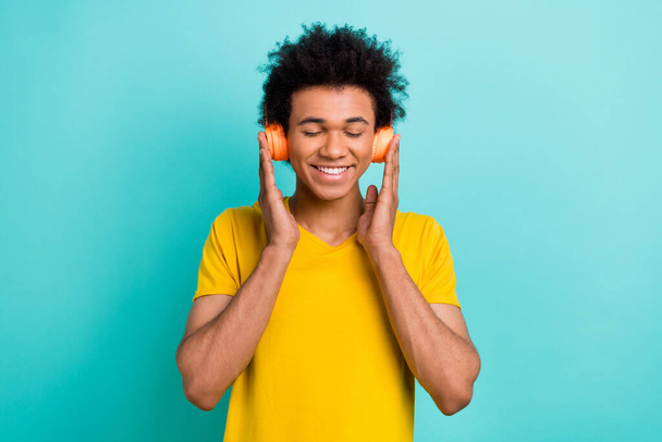 Photo of cheerful relaxed peaceful guy wear yellow t-shirt hands touching headphones enjoy playlist isolated on turquoise color background. - Photo, image