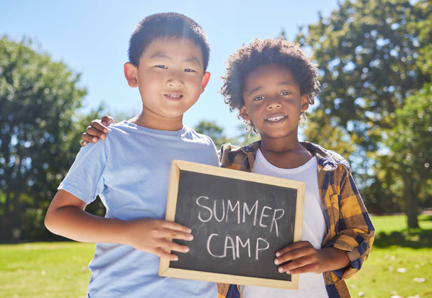 Summer camp, portrait or boys hugging in park together for fun bonding, development or playing in outdoors. Happy young best friends smiling or embracing on school holidays outside with board sign. - Foto, immagini