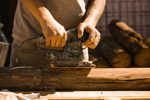 Craftsman's hands close up with old polishing machine on wooden logs. Working on wood with a special woodworking machine. Carpenter or engineer master working hard. Electric polisher, Orbital sander. - Φωτογραφία, εικόνα