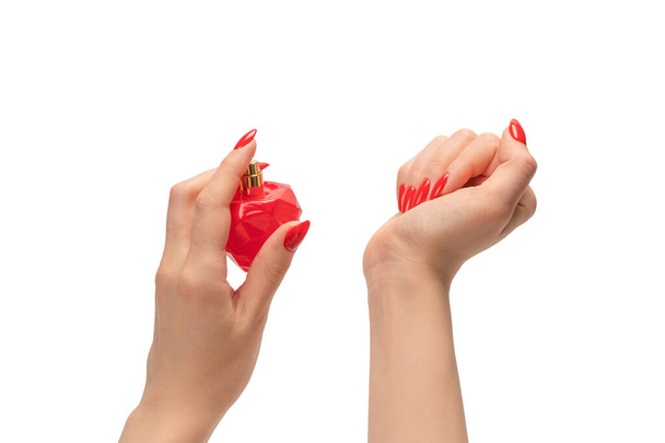 Červená láhev parfému v ruce ženy s červenými nehty izolované na bílém pozadí. Aplikace parfému. - Fotografie, Obrázek