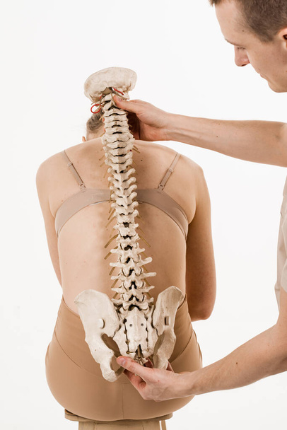 Orthopedist showing spinal column model with girl on white background. Scoliosis is sideways curvature of the spine. Backbone anatomical model with young woman - Foto, Imagen