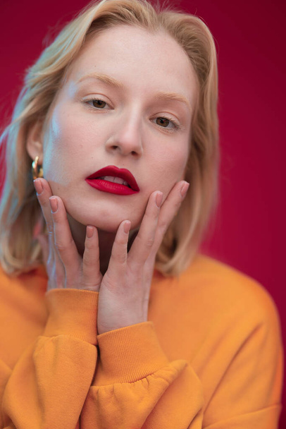 Studio shot of a serious blond woman posing on red background. - 写真・画像