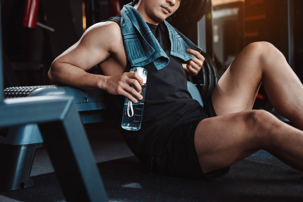 Man exercise workout in gym fitness breaking and resting after training sport with dumbbells and water bottle healthy lifestyle bodybuilding. - Photo, Image