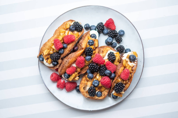Fresh sweet rolls with cream cheese and fresh blueberries, strawberries, raspberries and currants on a white plate on a white-grey stripped surface. Copyspace. Bakery advertisement. Food advertisement - Foto, Bild