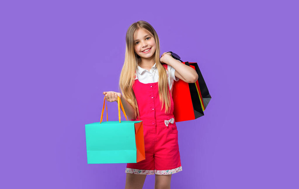 happy teen girl with shopping purchase isolated on purple. teen girl with shopping purchase in studio. teen girl with shopping purchase on background. photo of teen girl with shopping purchase. - Zdjęcie, obraz