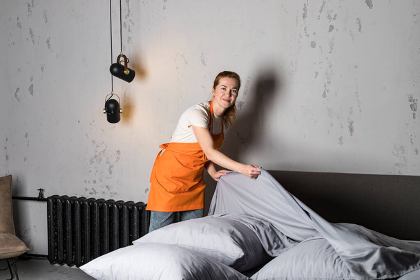 Eine Frau in Schürze vom Reinigungsdienst macht das Bett. Reinigung von Möbeln. - Foto, Bild