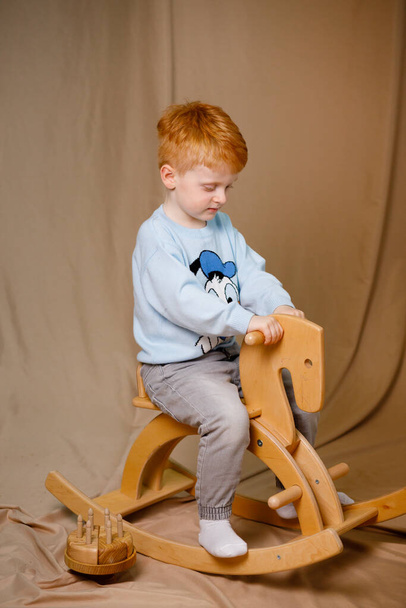 Un ragazzo dai capelli rossi con un maglione blu gioca con i giocattoli di legno. Sfondo marrone - Foto, immagini