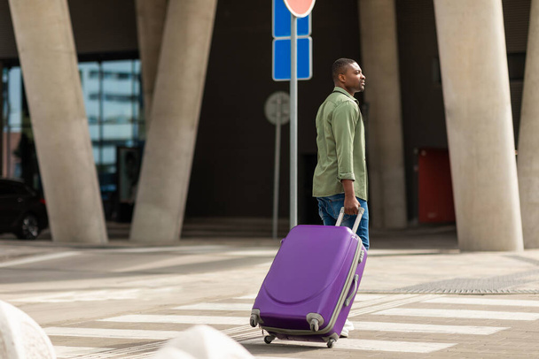 Afroameričan Traveler Man Walking With Suitcase Through Crosswalk Near Modern Airport Building Přílet před jeho letem. Full Length Of Male Passenger Crossing Road. Cestování a doprava - Fotografie, Obrázek
