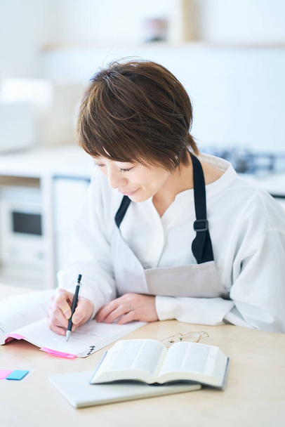 Женщина в фартуке, изучающая текст на кухне - Фото, изображение