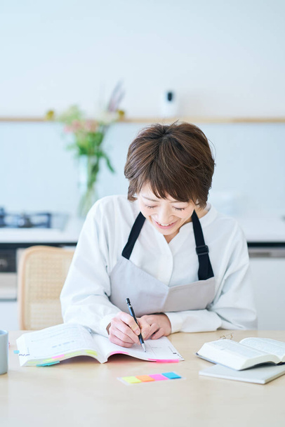 Une femme dans un tablier étudiant par texte à la cuisine - Photo, image