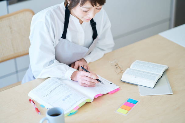 A woman in an apron studying by text at kitchen - Photo, Image