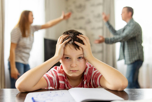 Een zoon voelt zich gefrustreerd terwijl zijn ouders op de achtergrond vechten. Gezinsconflicten of echtscheidingsgevolgen voor de ontwikkeling van kinderen - Foto, afbeelding
