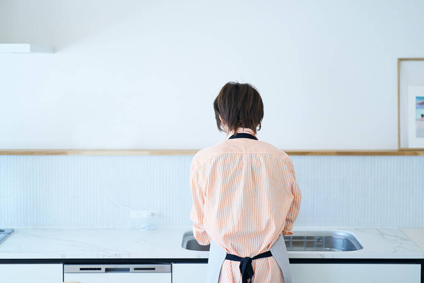 Rear view of a woman washing dishes in the kitchen - 写真・画像
