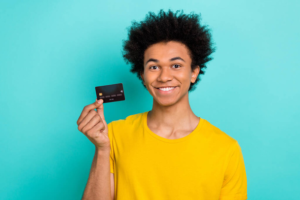 Portrait of satisfied good mood guy afro hairdo wear yellow t-shirt fingers hold plastic card isolated on shine teal color background. - Фото, зображення
