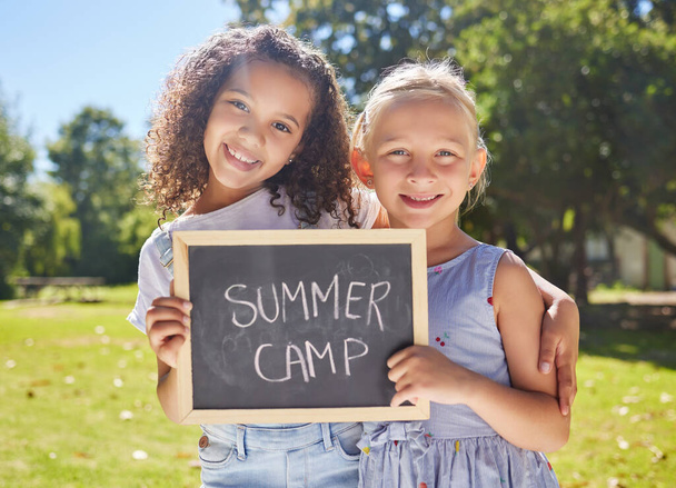 Summer camp, portrait or girls hugging in park together for fun bonding, development or playing in outdoors. Happy young best friends smiling or embracing on school holidays outside with board sign. - Foto, immagini