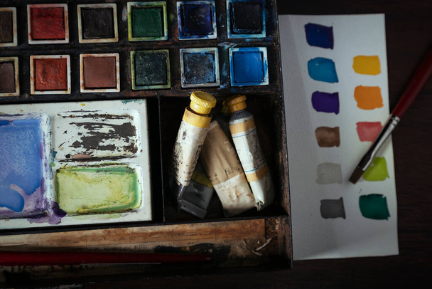 A vintage water color set in a metal tin sitting on a dark wood desk with color swatches on watercolor paper - Foto, Imagem