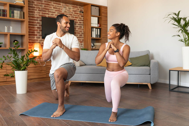 Smiling handsome young black lady and guy in sportswear doing leg exercises on workout, enjoy fit, energy and sport in living room interior. Stretch, body care, weight loss and active fitness at home - Photo, Image