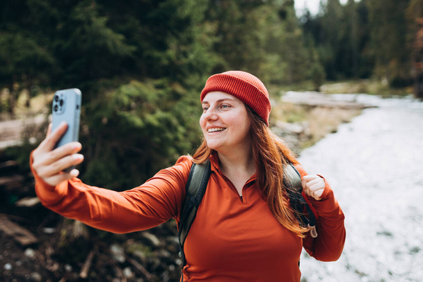 Woman in hat uses a telephone for take pictures, makes selfies and video calls family from home on mountains background. Travel and wanderlust concept. Chill moment - Foto, Imagen