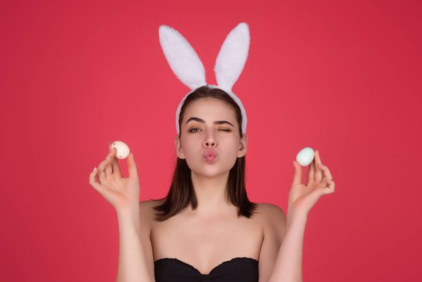Cheerful young woman wearing Easter bunny ears holding decorative colored eggs on studio background with copy space - Foto, afbeelding