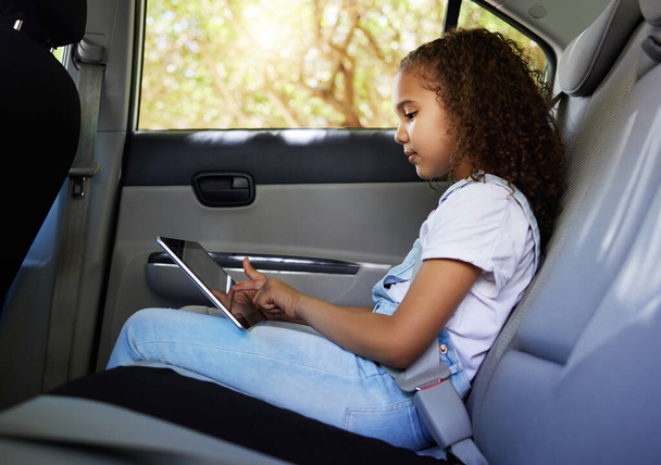 Child in car, tablet and road trip with seatbelt for safety and device to watch educational video or online game. Technology, internet and summer travel, happy girl on backseat for drive or carpool - Photo, Image