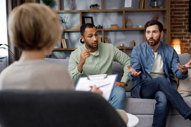 A family psychologist conducts a session in a beautiful office. LGBT couple at a psychotherapists appointment. Psychologist for gays. Support for the LGBT community in visiting a psychologist - Foto, imagen