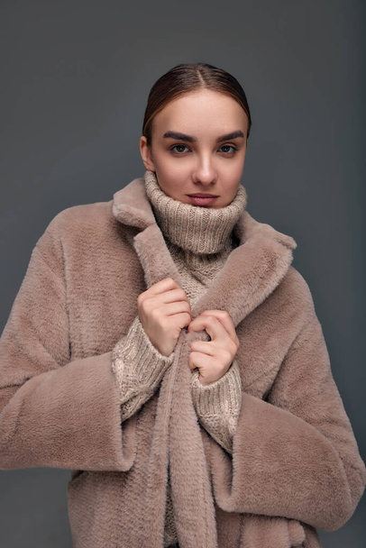 Mode jeune femme dans un manteau en fausse fourrure sur un fond gris - Photo, image
