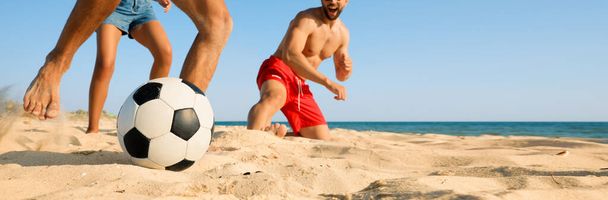 Baráti társaság focizik a homokos parton, alacsony látószögű kilátással. Bannertervezés szöveges szöveggel - Fotó, kép