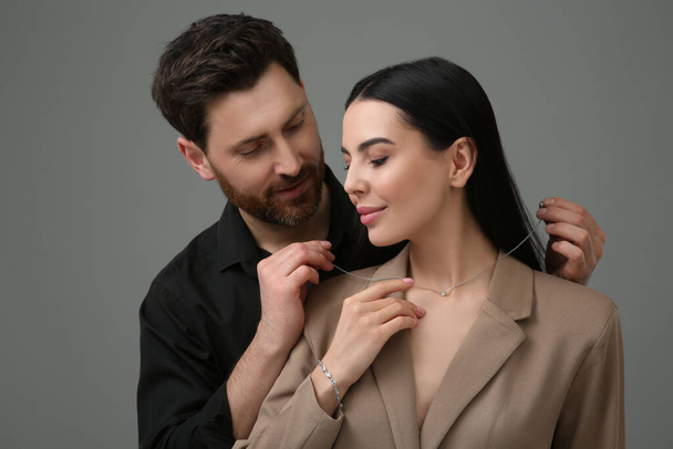 Man putting elegant necklace on beautiful woman against dark grey background - Fotoğraf, Görsel