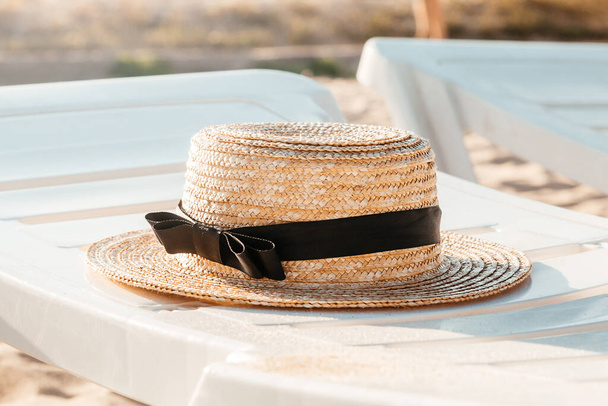 Straw hat on the white deck on the beach. Lounge chair next to a sea. Summer, vacation background - Фото, изображение