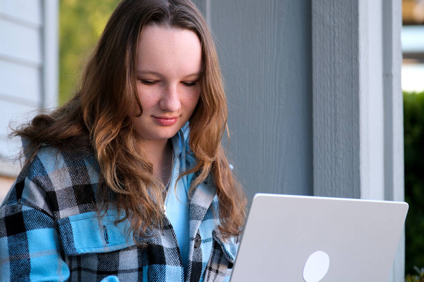 dospívající dívka s laptopem sedícím na verandě domu. Ona se dívá na zprávy dělá domácí úkol on-line konference batoh složka vody láhev tužka obyčejní lidé skutečný život - Fotografie, Obrázek