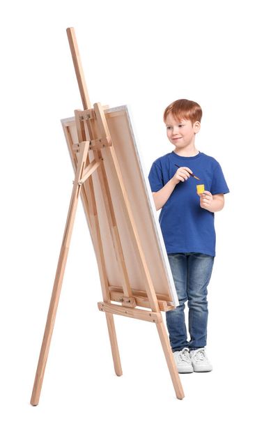 Mały chłopiec maluje na białym tle. Używając sztalugi do trzymania płótna - Zdjęcie, obraz