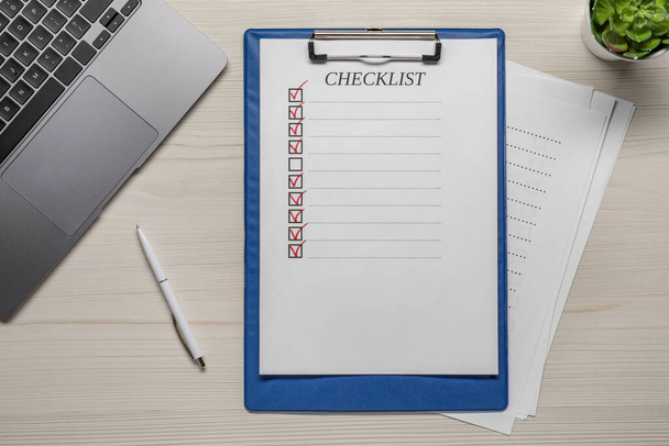 Clipboard with checklist, pen and laptop on wooden table, flat lay - Fotoğraf, Görsel