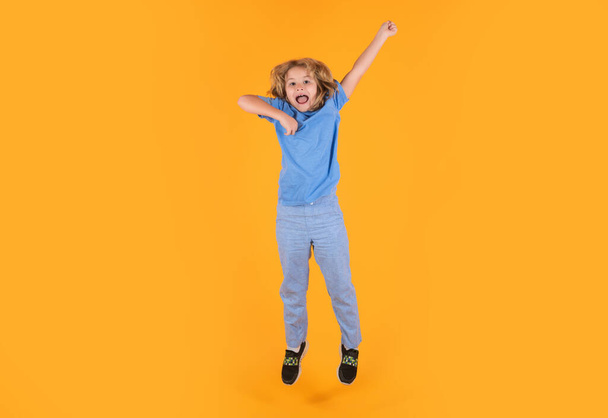 Фотография мальчика в полный рост, прыгающего высоко в случайной чеканной рубашке на желтом фоне. Портрет прыгающего мальчика. Прыжки детей, веселье - Фото, изображение