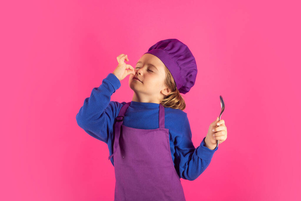 Funny kid chef cook with spoon. Kid chef cook prepares food on isolated studio background. Kids cooking. Teen boy with apron and chef hat preparing a healthy meal - Φωτογραφία, εικόνα