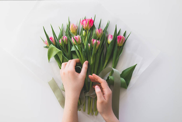 Naisten kädet tilalla kimppu kaunis herkkä tulppaani kukkia valkoisella pohjalla. Kimppu vaaleanpunainen tuore tulppaanit. - Valokuva, kuva