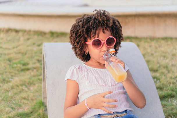 Chica con el pelo rizado sentado en un banco del parque beber jugo - Foto, imagen