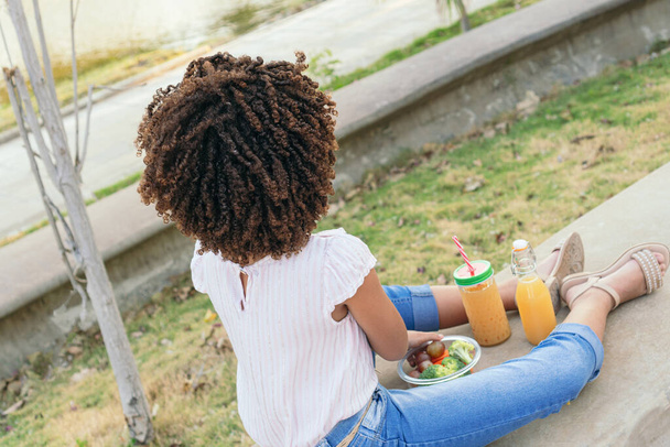 Dziewczyna z kręconymi włosami jedząc warzywa podczas siedzenia w parku w lecie - Zdjęcie, obraz