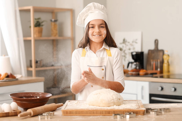 Маленький пекарь поливает тесто мукой за столом на кухне - Фото, изображение