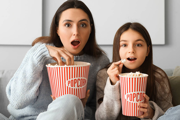 Pieni tyttö ja hänen äitinsä lämpimissä villapaidoissa popcornin kanssa katsomassa televisiota kotona - Valokuva, kuva