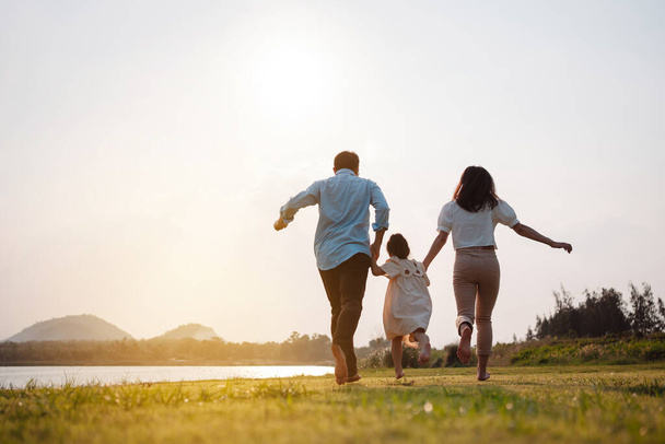 Happy family in the park sunset light. family on weekend running together in the meadow with river Parents hold the child hands.health life insurance plan concept. - Foto, Imagem