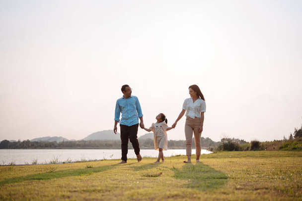 Happy family in the park sunset light. family on weekend running together in the meadow with river Parents hold the child hands.health life insurance plan concept. - Foto, imagen