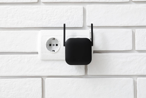 répéteur WiFi noir en prise électrique sur mur de briques blanches - Photo, image