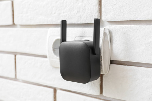 Repetidor WiFi preto em tomada elétrica na parede de tijolo branco - Foto, Imagem