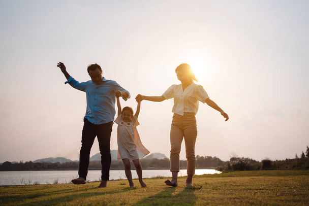Happy family in the park sunset light. family on weekend running together in the meadow with river Parents hold the child hands.health life insurance plan concept. - 写真・画像