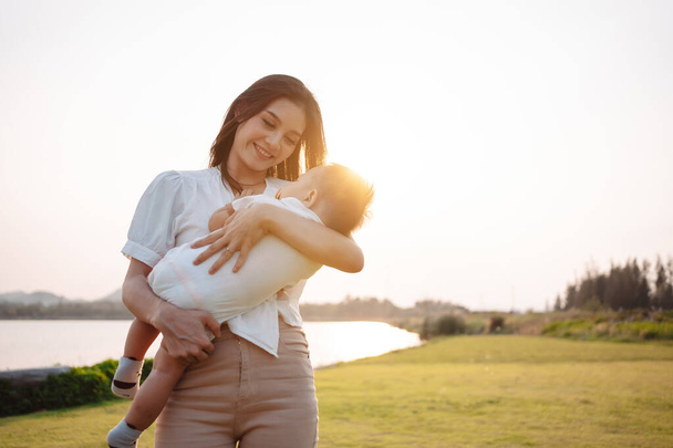 Mother Parenting and newborn birth life. Mom and baby boy playing in park sunset, Family having fun together. childcare, maternity concept. - 写真・画像