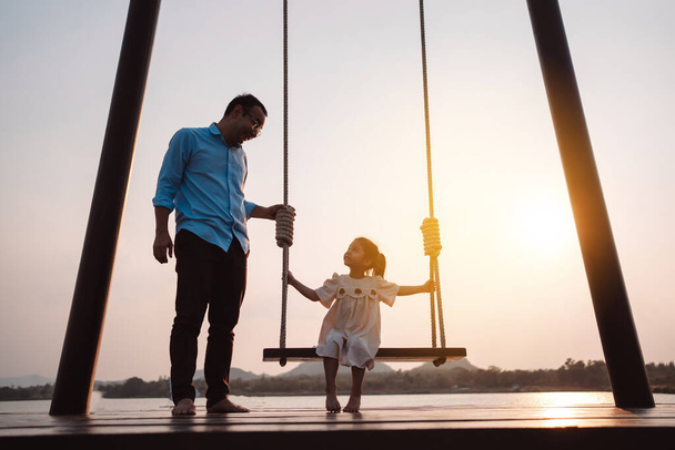 Happy family enjoying with swing in the park at sunset outdoor in nature, Weekend activity of family life together. - 写真・画像